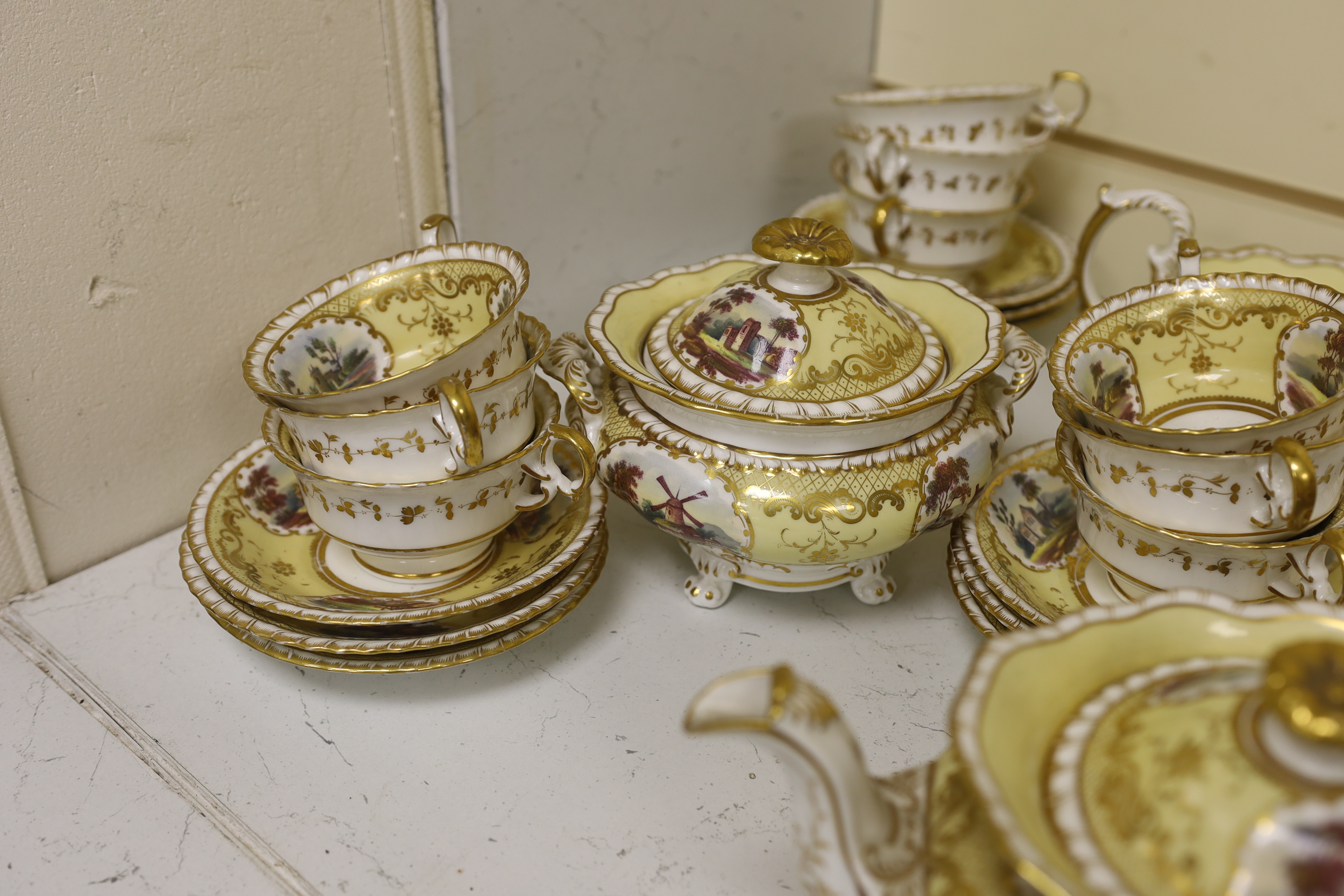 An English porcelain tea set, c.1835-45, including a teapot and cover, sucrier and cover, slops bowl, milk jug, teacups and saucers, two cake plates, each piece painted with buildings in landscapes, yellow ground, patter